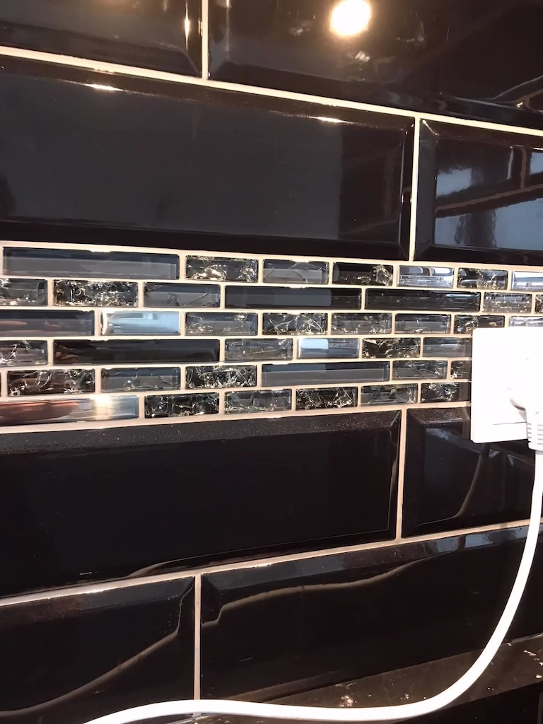 Opas w kuchni wykonany z czarnej płytki typu cegła i szklanej mozaiki. Fuga w kolorze jasnoszarym podkreśla zarysy szklanej mozaiki i eksponuje głębie czarnej płytki.